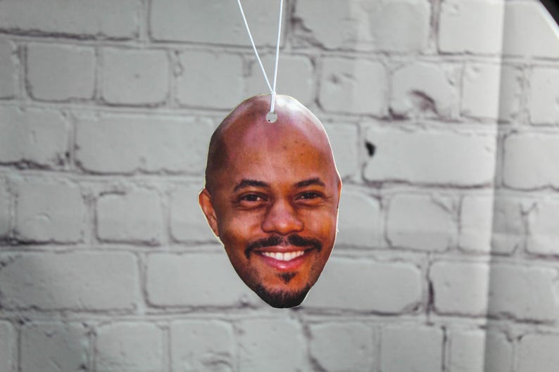 Puede incluir: Un ambientador de coche con una foto de primer plano de la cara de un hombre sonriendo.