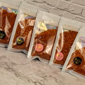 Peut inclure: Cinq sachets en plastique transparent remplis d'un mélange d'épices rouge-orange. Chaque sachet porte une petite étiquette ronde avec le texte "Merci pour votre commande" en lettres dorées.