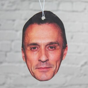 Puede incluir: Un ambientador de coche con una foto de primer plano de la cara de un hombre. El hombre tiene el pelo corto y casta&ntilde;o y mira directamente a la c&aacute;mara.