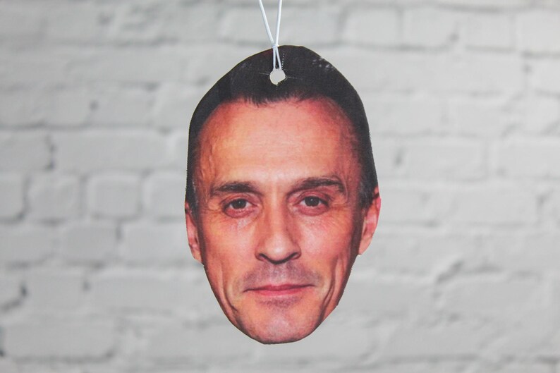 Puede incluir: Un ambientador de coche con una foto de primer plano de la cara de un hombre. El hombre tiene el pelo corto y casta&ntilde;o y mira directamente a la c&aacute;mara.