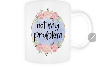 May include: White ceramic mug with a blue watercolor background and a gold circle around the text "not my problem". The circle is surrounded by pink and white flowers.
