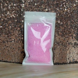 May include: A clear plastic pouch filled with pink bath salts. The pouch is sealed and ready to be used.