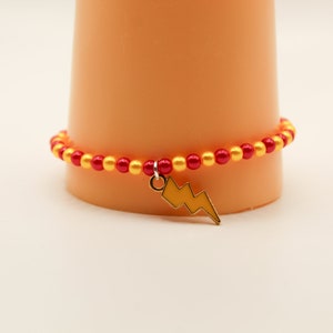 Op de afbeelding: Rode en gouden kralen armband met een gouden bliksem charme.