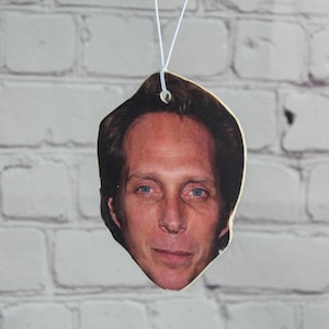 Puede incluir: Primer plano de un ambientador de coche con una foto de un hombre con cabello casta&ntilde;o y una expresi&oacute;n seria.