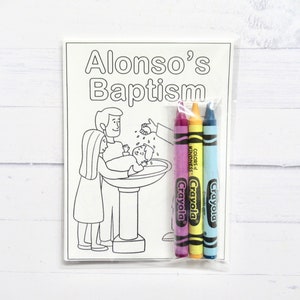 May include: A black and white coloring page with a scene of a baptism. The page is titled "Alonso's Baptism". The image shows a baby being baptized by a person pouring water from a pitcher. There are three crayons included in a plastic bag.