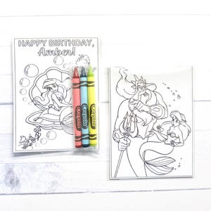 Puede incluir: Dos p&aacute;ginas para colorear en blanco y negro con Ariel y el Rey Trit&oacute;n de La Sirenita. Una p&aacute;gina tiene el texto "HAPPY BIRTHDAY, Amber!" con Ariel en una concha. Se incluyen tres crayones Crayola rojos, azules y amarillos.