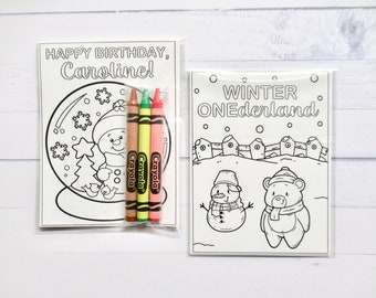 May include: Two rectangular coloring sheets in clear plastic sleeves. The left sheet features a snow globe with a snowman and the text "HAPPY BIRTHDAY, Caroline!" with three Crayola crayons. The right sheet shows a bear and snowman with "WINTER ONEderland".