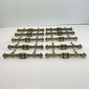 May include: A collection of antique brass drawer pulls. Each pull features a cylindrical center section with decorative end caps and mounting screws. The hardware has a vintage aesthetic, suitable for furniture restoration or adding a classic touch to cabinetry.