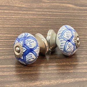 May include: Two decorative cabinet knobs. Each knob is a white ceramic sphere with a blue geometric pattern. The knobs have silver-colored metal bases and are designed for easy installation. The knobs are a stylish addition to any cabinet or drawer.