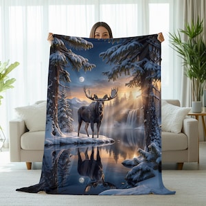 May include: A plush blanket featuring a serene winter landscape with a moose standing near a lake. The design includes snow-covered trees, a waterfall, and a full moon. The color palette is dominated by blues, whites, and golden hues.