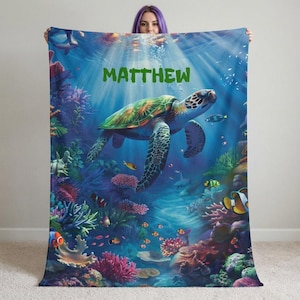 May include: A blue blanket featuring an underwater scene with a sea turtle, fish, and coral. The name "MATTHEW" is printed in green across the top. The blanket has a vibrant, colorful design.