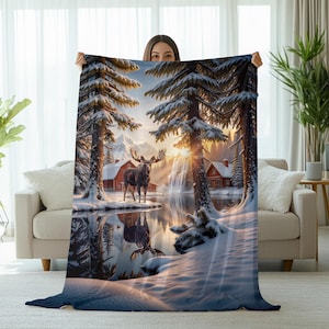 May include: A cozy blanket featuring a winter landscape with a moose standing near a lake. The scene includes snow-covered trees, a waterfall, and cabins, all bathed in the warm glow of the setting sun. The blanket is a soft, inviting home decor item.