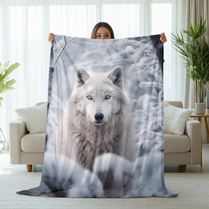 May include: A white wolf with blue eyes stands in a snowy forest. The wolf is looking directly at the camera. The background is a snowy forest with trees and branches covered in snow.