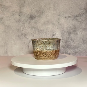 May include: A speckled brown and gray ceramic bowl with a white base sits on a white turntable.
