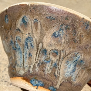 Könnte beinhalten: Eine Keramikschüssel mit brauner Glasur und blauen und weißen Marmorierungen. Die Schüssel hat eine einzigartige, organische Form und eine strukturierte Oberfläche.