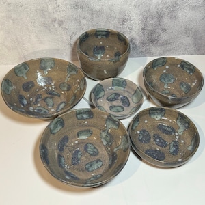 May include: Set of six ceramic bowls with a speckled brown and blue glaze. The bowls are various sizes and shapes, with some having a round shape and others having a more oval shape.