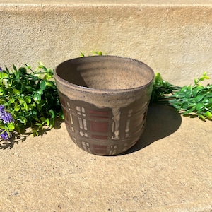 Puede incluir: Una maceta de cerámica marrón con un patrón geométrico en tonos marrones, rojos y blancos.