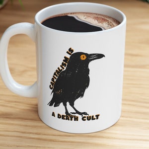 May include: White ceramic mug with a black crow illustration and the text "Capitalism is a death cult".