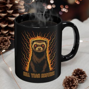 May include: Black ceramic mug featuring a cartoon ferret with fiery accents and the text "HELL YEAH BROTHER." The mug has a curved handle and is filled with a dark liquid, possibly coffee or tea.