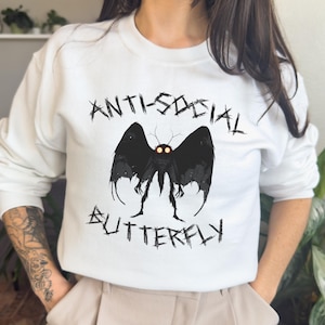May include: White sweatshirt with a black and white graphic of a butterfly with the text "Anti-Social Butterfly" printed on it.