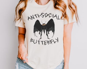 Puede incluir: Una camiseta blanca con un gráfico negro de una polilla con el texto "Anti-Social Butterfly" en negro.