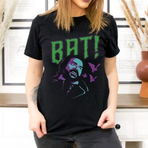 May include: Black t-shirt featuring a green and purple graphic of a bearded man with the text "BAT!" printed on it.