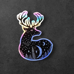 May include: A holographic sticker featuring a black silhouette of a deer with antlers, surrounded by stars and crescent moons. The deer is looking to the left, and the background is a dark blue with a hint of purple.