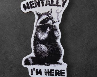 Puede incluir: Una pegatina en blanco y negro con un mapache fumando un cigarrillo. El mapache sostiene el cigarrillo con sus patas. El texto "MENTALLY" está encima del mapache y "I'M HERE" debajo.