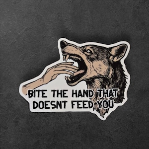 May include: A sticker featuring a wolf biting a hand, with the text "BITE THE HAND THAT DOESN'T FEED YOU." The wolf is depicted in shades of brown and black, with a menacing expression. The hand is in a light skin tone.