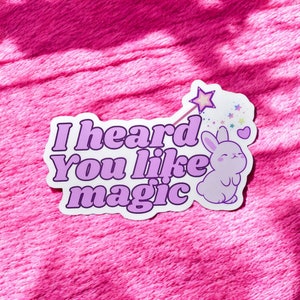 Puede incluir: Una pegatina blanca con un conejo rosa sosteniendo una varita mágica. La pegatina dice "He oído que te gusta la magia" en letras rosas.