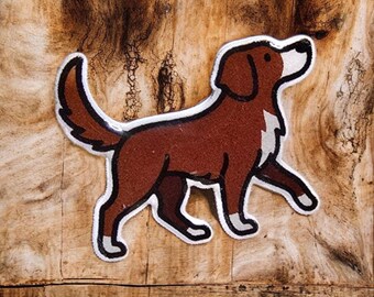 May include: A brown dog-shaped patch with white detailing and a black nose. The dog is walking right, tail up, with a white chest patch. The patch is outlined in white.