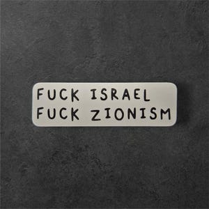 Pode incluir: Uma placa retangular esbranquiçada com cantos arredondados. O texto preto diz "FUCK ISRAEL" na linha superior e "FUCK ZIONISM" na inferior. O fundo é uma superfície cinza escuro texturizada.