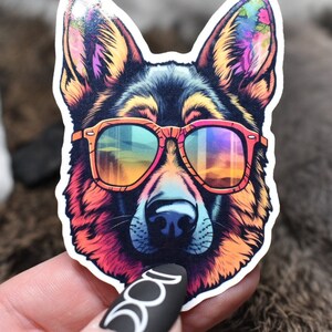 May include: A colourful sticker of a German Shepherd dog wearing rainbow-coloured sunglasses. The dog's fur is a mix of pink, orange, yellow, green, blue, and purple.