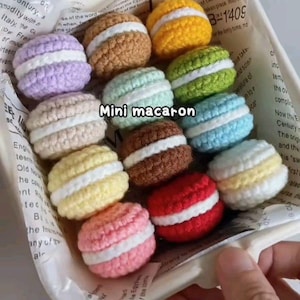 Könnte beinhalten: Eine Sammlung bunter, gehäkelter Mini-Macarons in einer weißen Schale. Die Macarons sind in verschiedenen Farben erhältlich, darunter Lila, Braun, Gelb, Grün, Blau, Rosa und Rot, mit weißer Füllung. Der Text "Mini macaron" ist sichtbar.