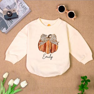 May include: A cream colored long-sleeved shirt with a pumpkin design and the name "Emily" printed on the front.