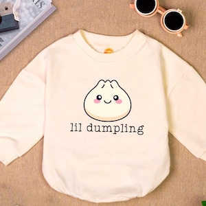 May include: A cream-colored long-sleeved shirt with a cartoon dumpling with a smiling face and the text "lil dumpling" printed on the front.