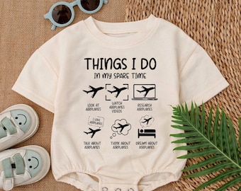 May include: A white baby onesie with black text that reads "Things I do in my spare time" and a list of activities related to airplanes. The activities include looking at airplanes, watching airplane videos, researching airplanes, talking about airplanes, thinking about airplanes, and dreaming about airplanes.