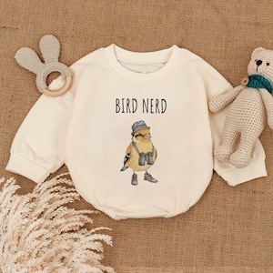 May include: A cream colored long-sleeved baby onesie with the text "BIRD NERD" printed on the front. A cartoon bird wearing a hat and binoculars is printed below the text.