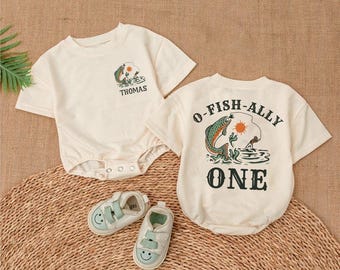 May include: Two cream-colored short-sleeved shirts with a fishing theme. One shirt says "O-Fish-Ally One" with a cartoon fish and the other says "Thomas".