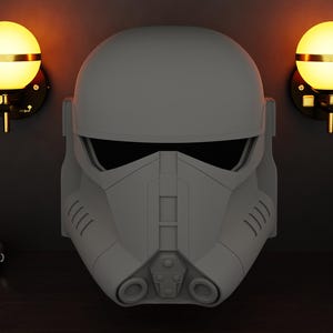 May include: A grey Stormtrooper helmet is the focal point of this image, set against a dark background. Two spherical wall sconces with gold accents flank the helmet. A decorative illustration of a helmet is in the upper left corner.