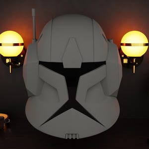 May include: A grey, angular helmet with a black visor, similar to a clone trooper helmet. The helmet is centered on a dark wooden surface, with two wall-mounted globe lights. A decorative illustration and a water bottle are also visible.