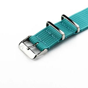 K&ouml;nnte beinhalten: Ein t&uuml;rkisfarbenes Nylon-Armband mit silberner Schlie&szlig;e und Halteschlaufen.