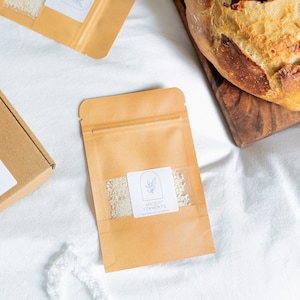 May include: A brown paper pouch with a white label that says "Ancient Ferments" and a small illustration of a plant. The pouch contains a white powder.
