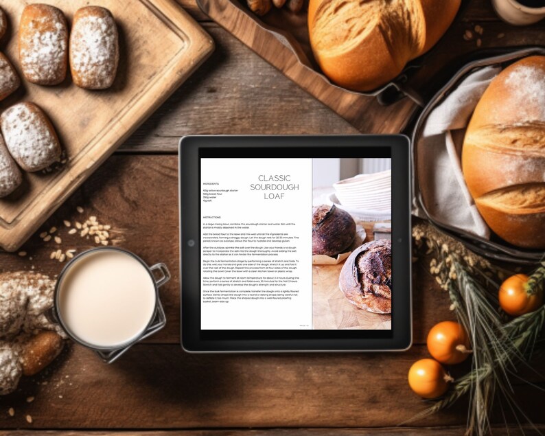 May include: Overhead shot of a wooden table with various baked goods. A tablet displays a recipe for a classic sourdough loaf. Several loaves of bread, rolls dusted with powdered sugar, and a glass of milk are arranged around the tablet.