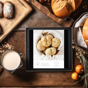 May include: A digital tablet displaying a book cover with the title "Gluten Free Sourdough" and the text "20 Inspiring Recipes for Sourdough Bakers" by Ancient Ferments. The cover features a basket of freshly baked sourdough rolls.
