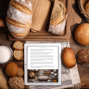 May include: A white tablet with a text about sourdough bread baking tools and techniques. The tablet is surrounded by various loaves of bread, a bowl of milk, and a basket of bread rolls on a wooden surface.