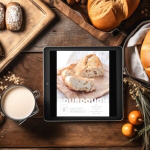 May include: Overhead shot of a wooden table with various baked goods. A tablet displays the word "SOURDOUGH" with the text "20 Inspiring Recipes for Sourdough Bakers." There are loaves of bread, rolls, and a glass of milk.