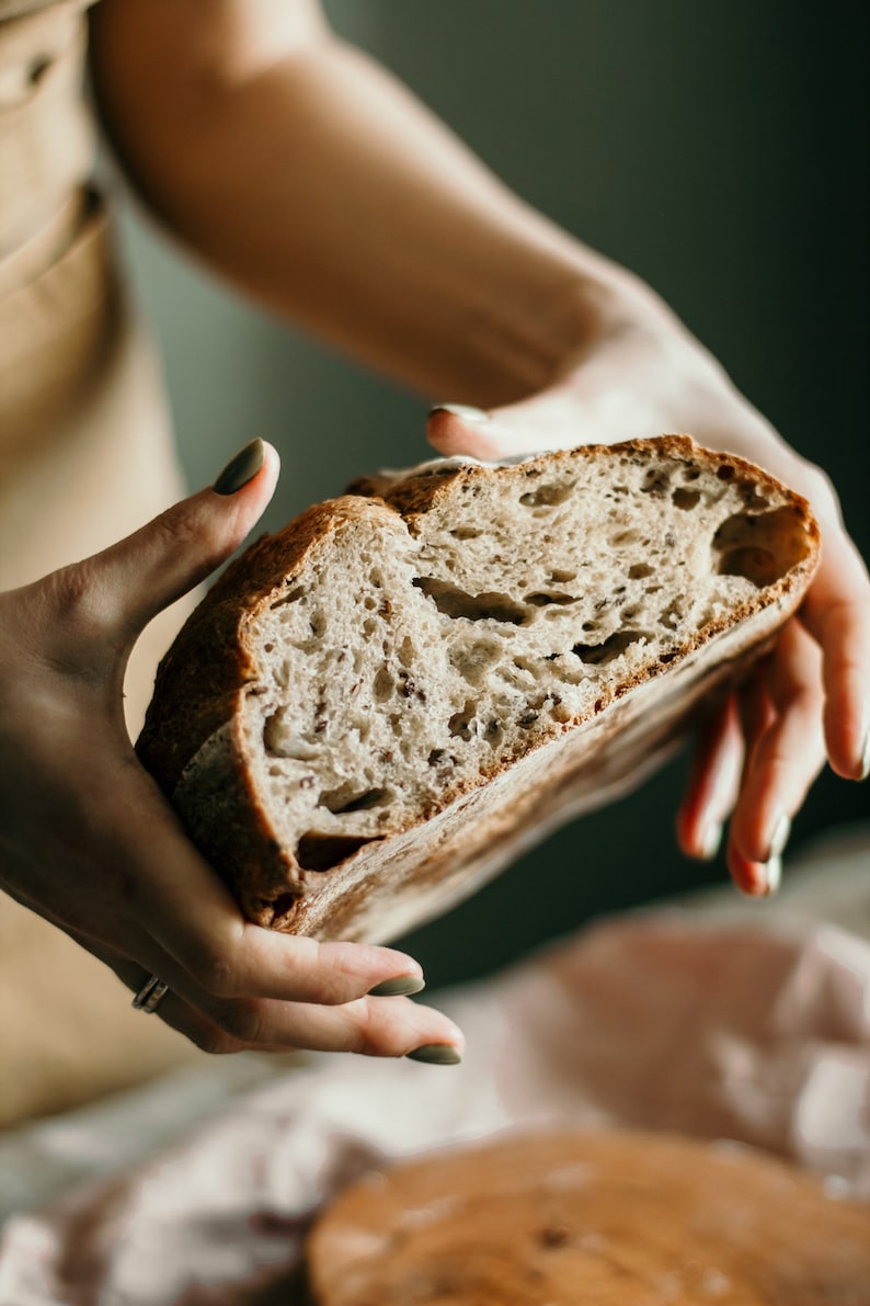 May include: A person holding a loaf of freshly baked sourdough bread with a rustic, crusty exterior and a soft, airy interior.