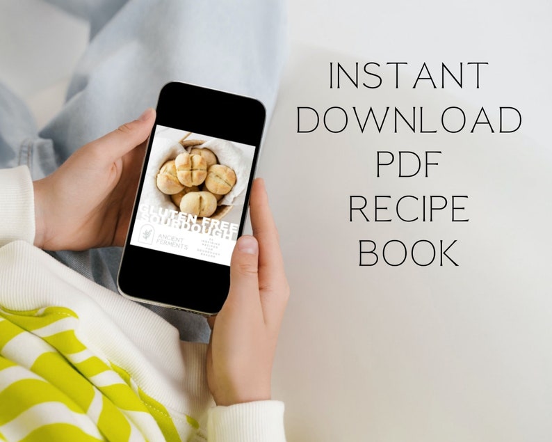 May include: A person is holding a smartphone displaying a digital recipe book for gluten-free sourdough bread. The text on the screen reads "Gluten-Free Sourdough" and "Ancient Ferments". The text on the white background behind the phone reads "INSTANT DOWNLOAD PDF RECIPE BOOK".