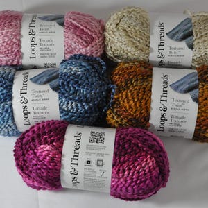 May include: Six skeins of Loops & Threads Textured Twist yarn in various colors, including pink, blue, beige, orange, and purple. The yarn is a blend of acrylic and is described as "Torsade Texture".
